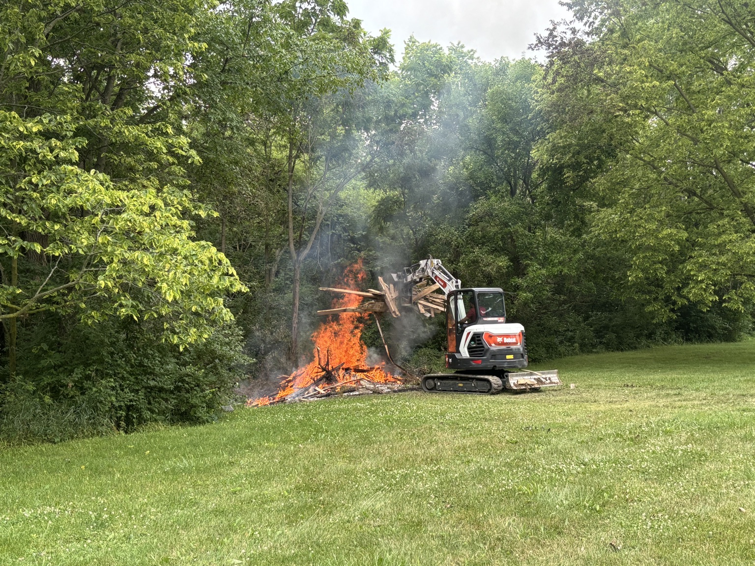 Excavator handling demolition debris at a wooded project site