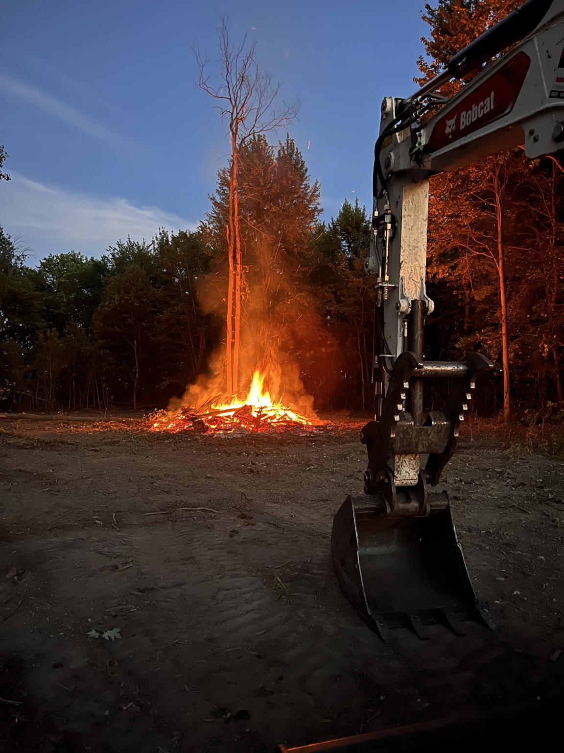 Brush clearing burn with excavator at a wooded site